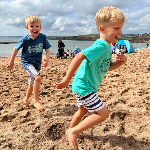 Boy running on the beach wearing a Jellymud aqua bamboo t-shirt featuring a John Aspden limited edition print