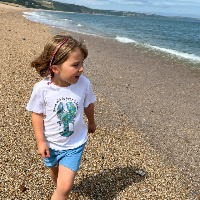 Girl walking on beach wearing a Jellymud white bamboo t-shirt, featuring a limited edition John Aspden lobster print.